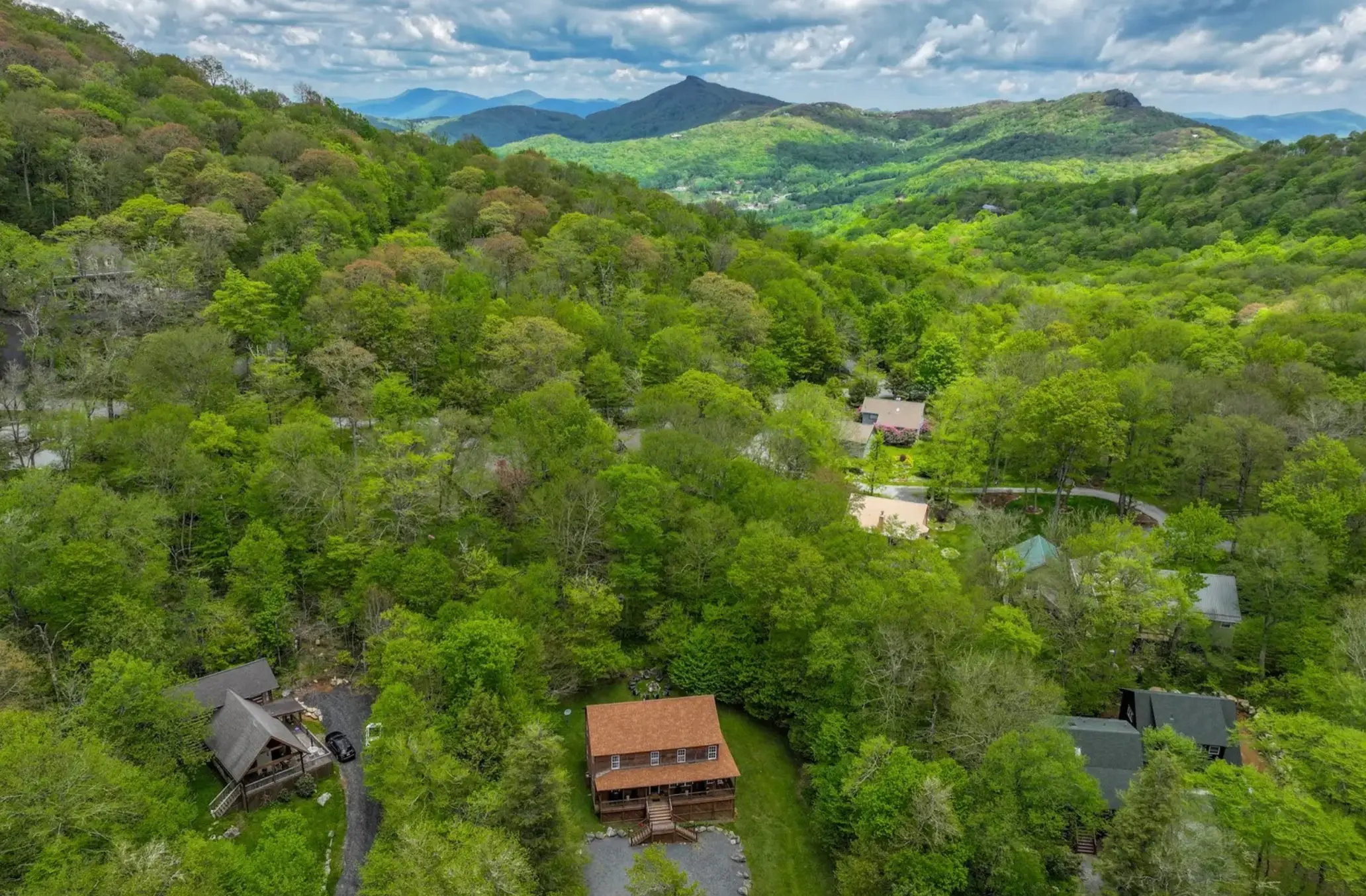 Aerial view of the home and its yard among wooded neighboring lots, with the valley and mountain ridges beyond.