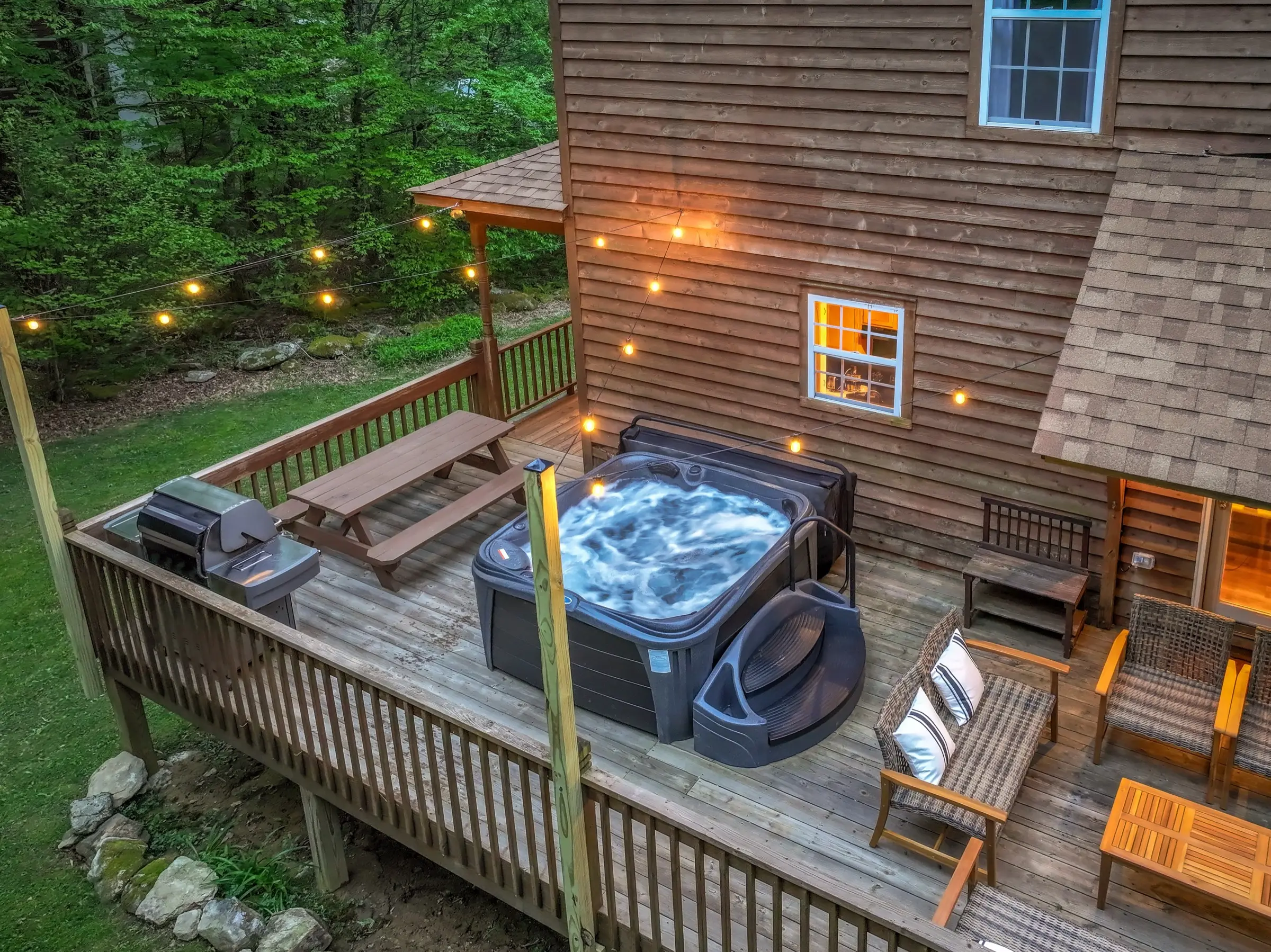 The rear deck from above: hot tub, propane grill, picnic table and wicker seating under string lights.