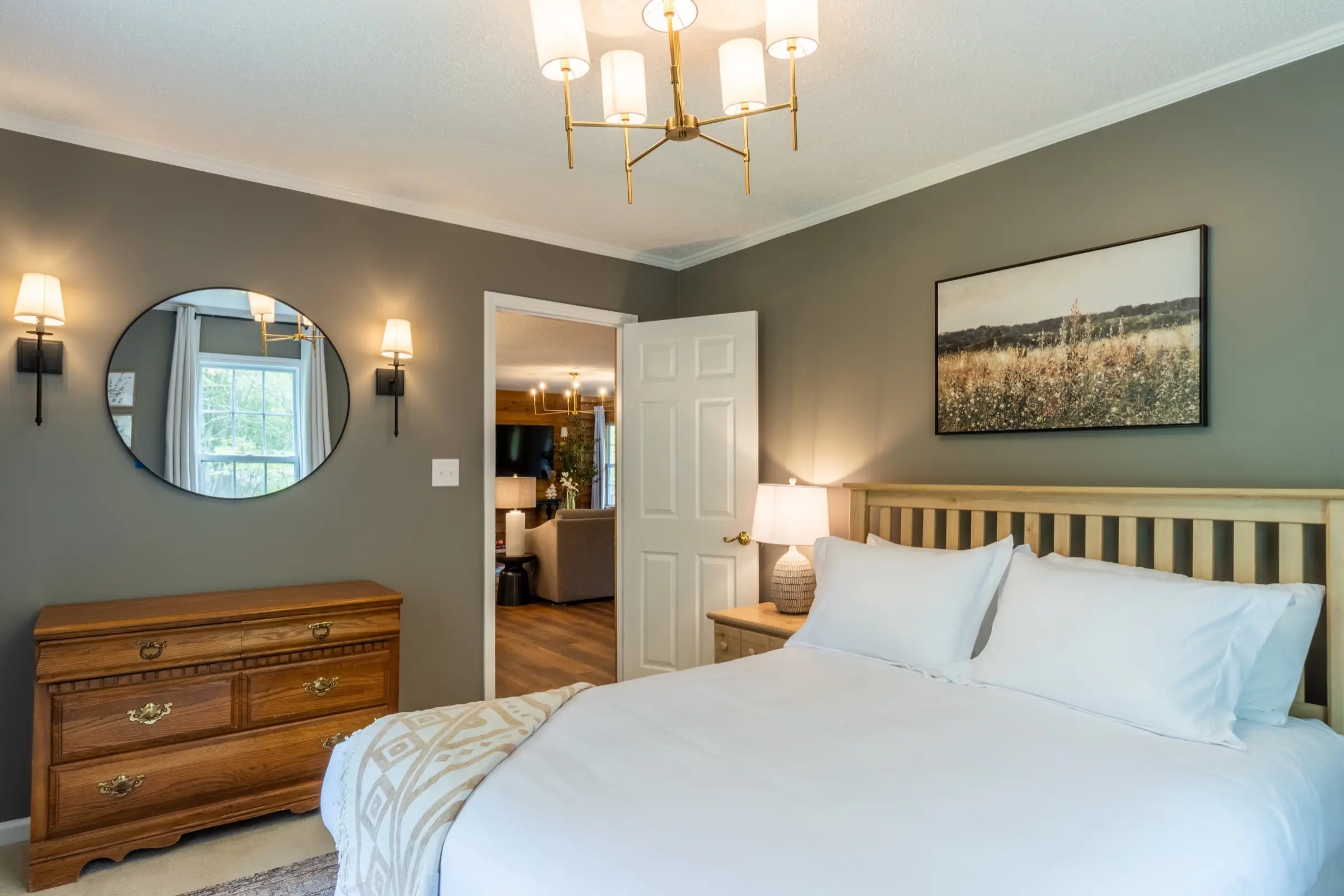Downstairs bedroom 2, with a queen bed and a round mirror above a wooden dresser.