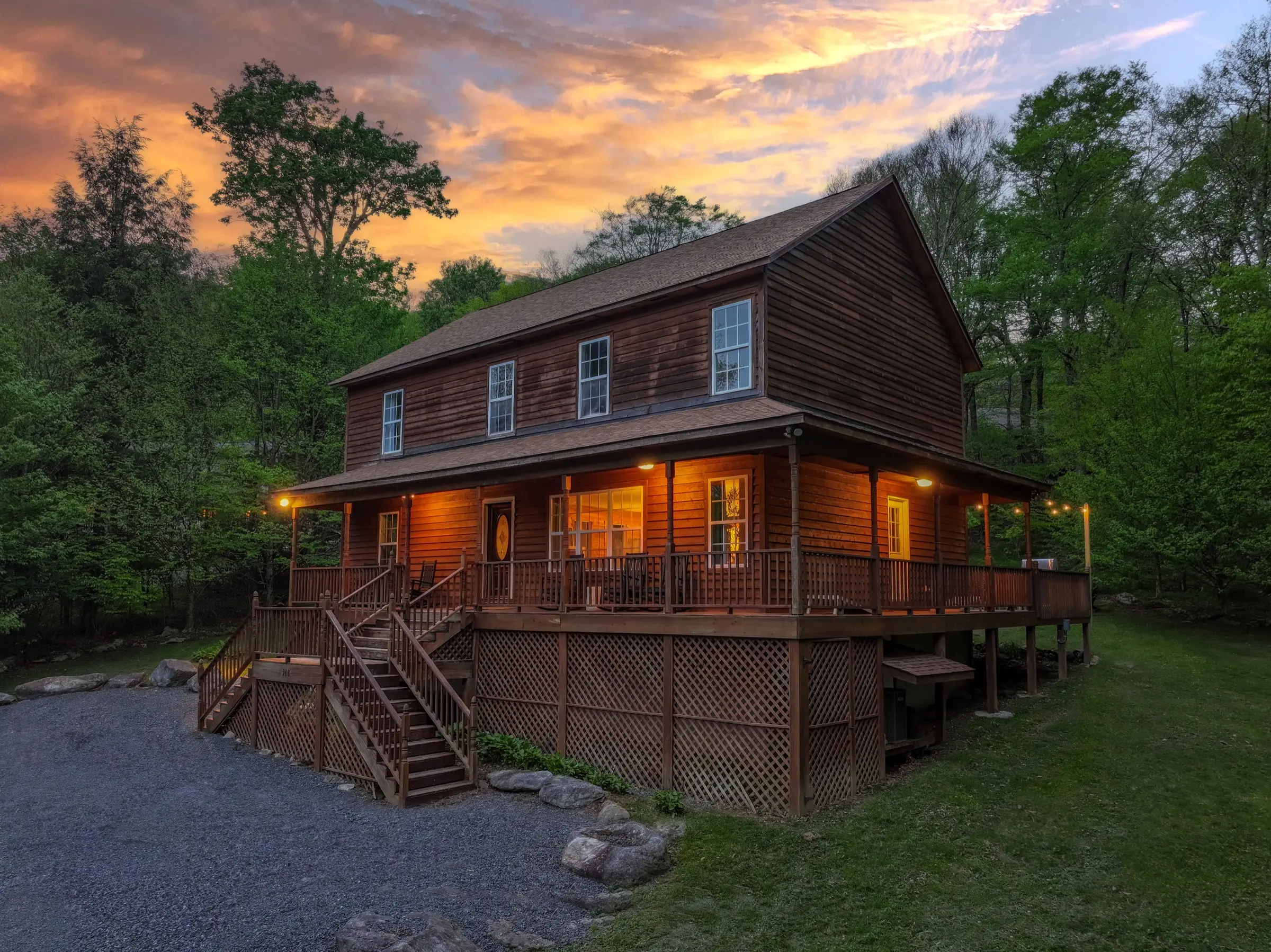 The front of the home at sunset, porch lit, with the gravel parking area in front.