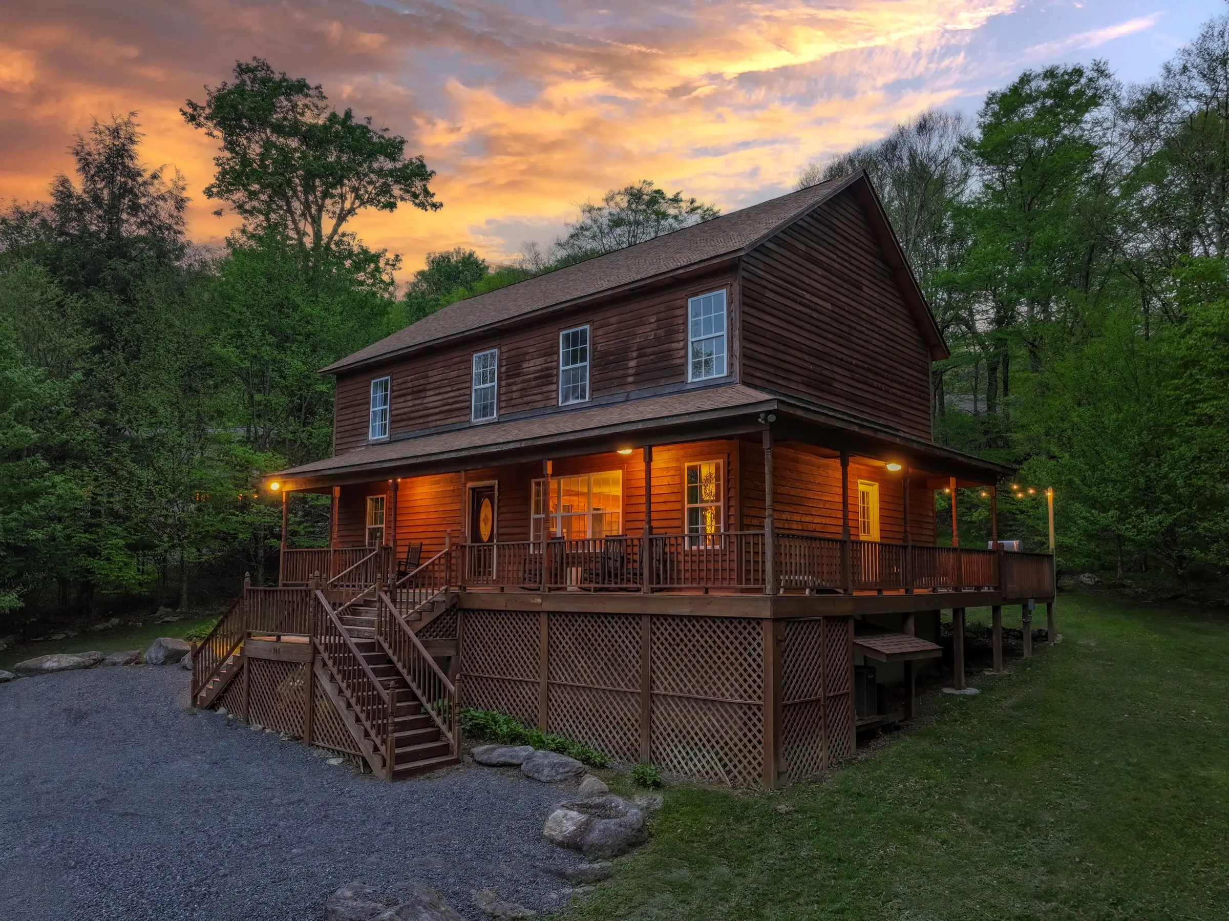 The front of The Sugar Nest at sunset, porch lit, with the gravel parking area in front.