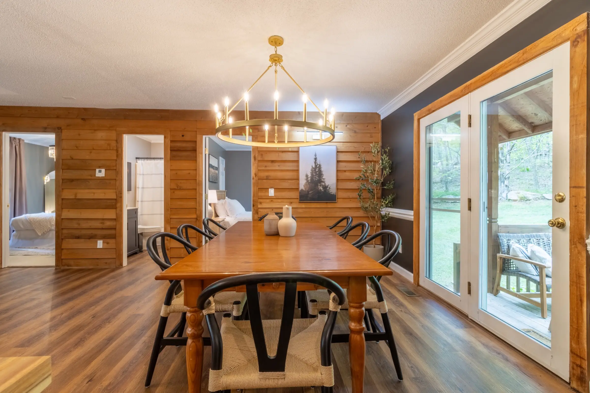 The dining table seating eight beneath a ring chandelier, with French doors to the deck.